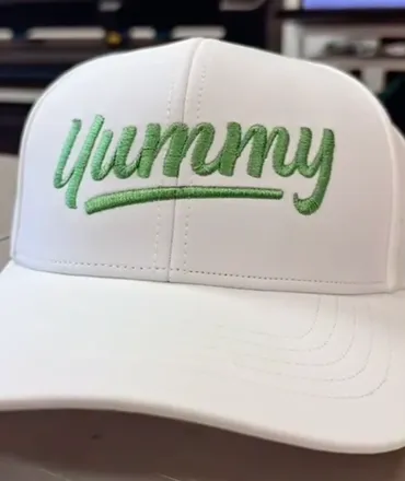 White cap embroidered with green Yummy lettering at Masters of Print