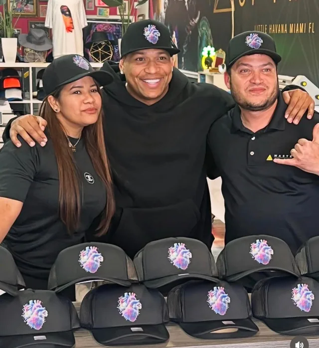 Three people posing behind a display of custom caps in the print shop